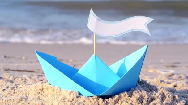 Bateau en papier bleu sur une plage de sable près de la mer par une journée d'été ensoleillée. — Video