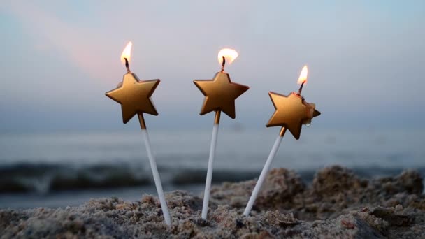 Três velas em forma de estrela queimam na areia na praia no fundo do mar borrado — Vídeo de Stock