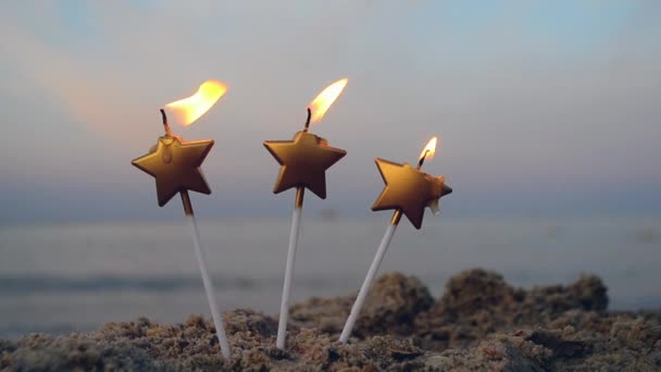 Три свічки у формі зірки горять у піску на пляжі на тлі розмитого моря — стокове відео