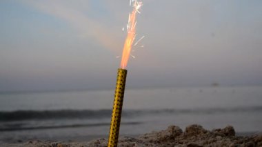 Sahilde kıvılcımlarla yanan tatil mumu, alacakaranlıkta denizin arka planında.