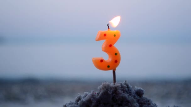 Свічка номер три вставлені пісок і опіки Освітлена свічка в піску на фоні — стокове відео