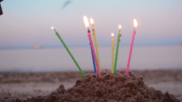 Brännande ljus för tårta i sand på bakgrund av suddiga havsvågor. — Stockvideo