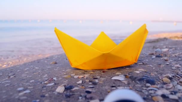 Kleine papieren gele boot op zand in de buurt van water op de achtergrond van zee golven close-up. — Stockvideo