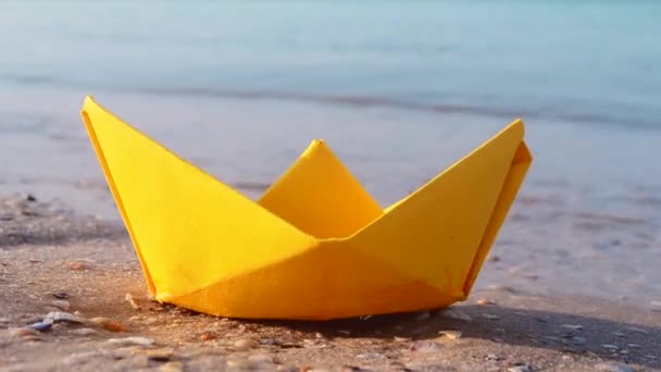 Small paper yellow boat on sand near water on background of sea waves close-up. — Vídeo de Stock
