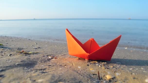 Small paper orange boat on sand near water on background of sea waves close-up. — Stockvideo