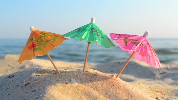 Бумажные коктейли разноцветные зонтики на песчаном морском пляже в солнечный летний день — стоковое видео