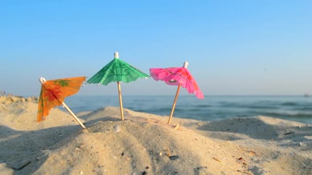 Бумажные коктейли разноцветные зонтики на песчаном морском пляже в солнечный летний день — стоковое видео