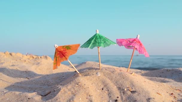 Papír koktél többszínű esernyők a homokos tengerparton a napos nyári napon — Stock videók