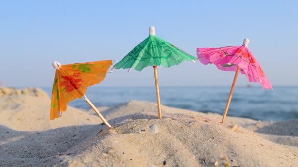 Paper cocktail multi-colored umbrellas on sandy sea beach on sunny summer day — Wideo stockowe