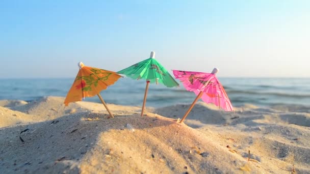 Paraguas multicolor de cóctel de papel en la playa de arena de mar en el soleado día de verano — Vídeos de Stock