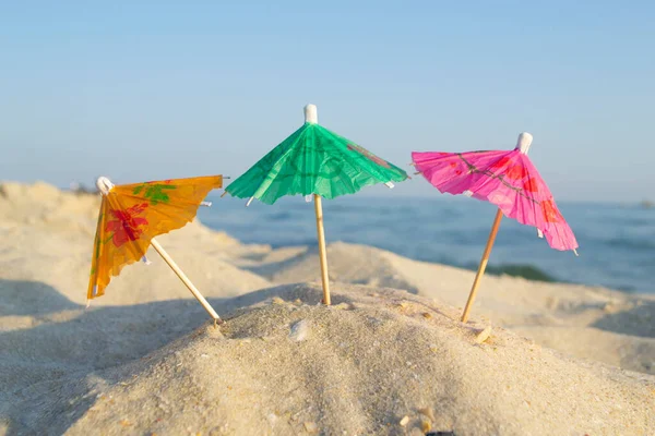 모래사장 가까이 모래 위에 서 있는 작은 종 이 칵테일 우산 세 개. — 스톡 사진