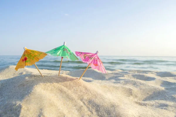 하얀 해변에 푸른 하늘을 가진 다양 한 색상의 우산 세 개 종이 칵테일 — 스톡 사진