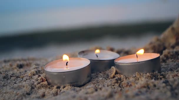 Три маленькі палаючі свічки на піску на тлі розмитих хвиль в сутінках — стокове відео