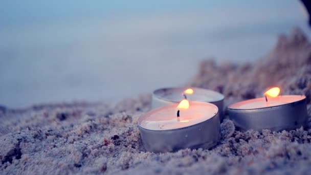 Tre piccole candele in fiamme su sabbia su sfondo di onde sfocate al crepuscolo — Video Stock