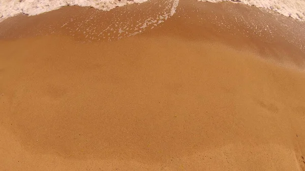 Havsvåg med vitt skum rullar över sandstranden. Ovanifrån. — Stockfoto