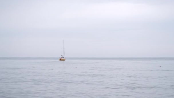 Морской пейзаж. Маленькая желтая яхта качается по волнам в пасмурную погоду. — стоковое видео
