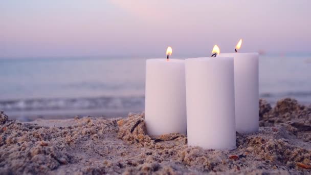 Tres grandes velas de parafina blanca se queman en el fondo de la playa de arena olas marinas — Vídeo de stock