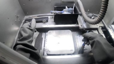 Plastik eldivenli erkek işçi, 3D yazıcının içindeki baskı platformunu metal için temizliyor