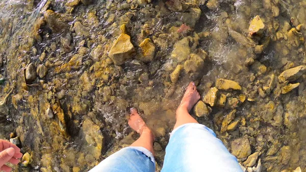 Flicka gå barfota på stenar av grunt flod närbild, solig sommardag — Stockfoto