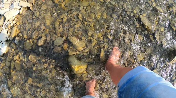 Meisje lopen blootsvoets op stenen van ondiepe rivier close-up, zonnige zomerdag — Stockfoto