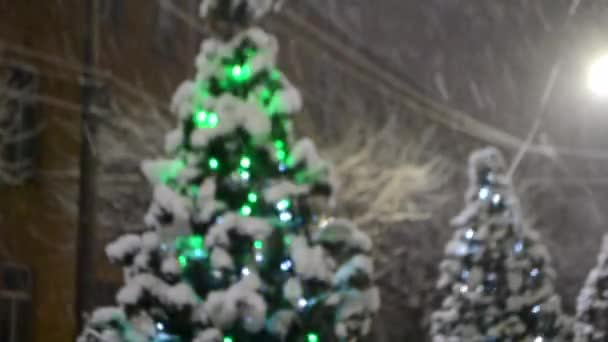 Árbol de Navidad cubierto de nieve, brillantes luces de colores durante las nevadas al aire libre. — Vídeo de stock