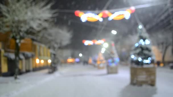 Θολή φόντο χιονισμένο δρόμο της πόλης με χριστουγεννιάτικα δέντρα και φωτισμό — Αρχείο Βίντεο