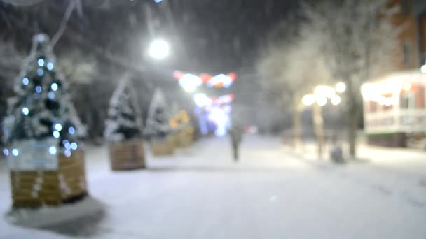 Yılbaşı ağaçları ve aydınlatma ile karlı şehir sokağının bulanık arka planı — Stok video