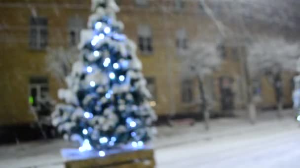 Árvore de Natal coberto de neve, brilhando luzes coloridas durante a queda de neve ao ar livre. — Vídeo de Stock