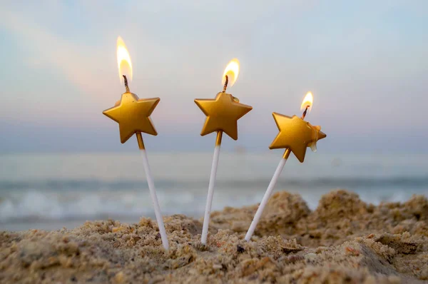 Three candles form of star burn in sand on beach on background — Stock Photo, Image