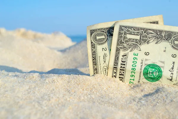 Twee oude dollarbiljetten in zand op de achtergrond van zeeblauwe lucht op zonnige zomer — Stockfoto