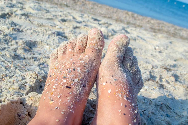 Dos pies desnudos de mujer caucásica manchada de arena con roca de concha en el mar arenoso —  Fotos de Stock