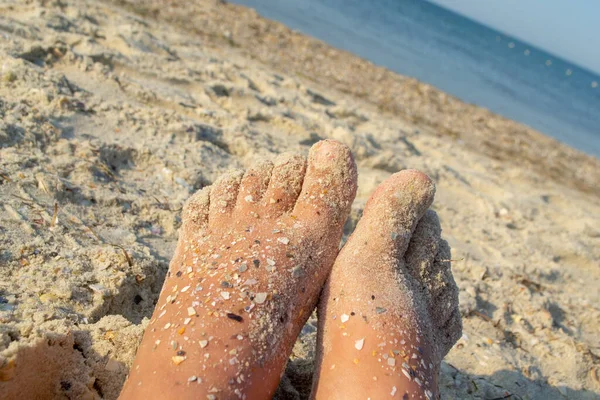 Two bare feet of caucasian woman soiled in sand with shell rock on sandy sea — Stock Photo, Image