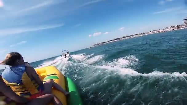 Persone che cavalcano sull'acqua attrazione gonfiabile con barca a motore Banana in mare — Video Stock