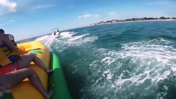 Persone che cavalcano sull'acqua attrazione gonfiabile con barca a motore Banana in mare — Video Stock