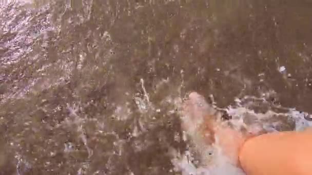 Dziewczyna z gołymi stopami spaceruje po wodzie po piaszczystej plaży morza i chlapie wodą — Wideo stockowe