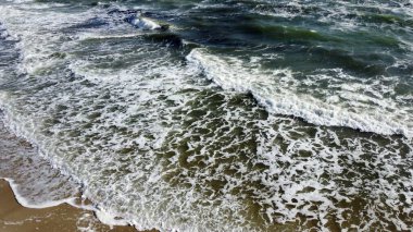 Kumlu sahile yuvarlanan deniz dalgaları üzerinde uçan hava aracı görüntüsü.