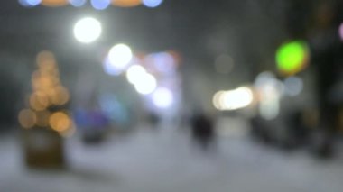 Arka plan bulanık. Kış gecesi kar yağarken şehir caddesi.