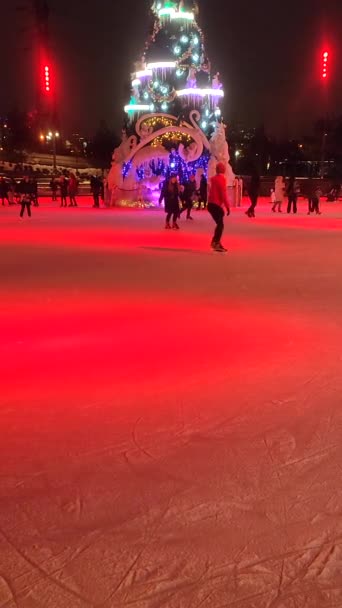 Ludzie jeżdżący na łyżwach na lodowisku z kolorowym światłem na świeżym powietrzu w zimie — Wideo stockowe