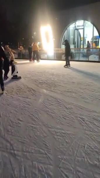 Gente patinando en una pista de patinaje sobre hielo con luz colorida al aire libre en invierno — Vídeo de stock