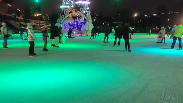 People skating on an ice skating rink with colorful light in open air — Stock Video