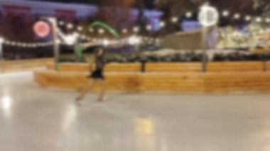Arka plan bulanık. Kız patenle kayıyor ve kurdeleyle artistik patinaj yapıyor.