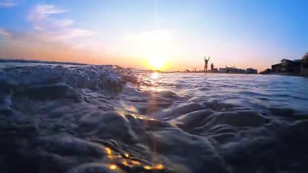 Muy bajo ángulo de tiro de las olas del mar estrellándose en la playa de arena. Gente caminando. — Vídeos de Stock