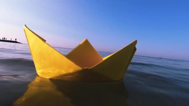 Sárga papírhajó úszik a felszínen a kék víz hullámok tenger közelkép. — Stock videók