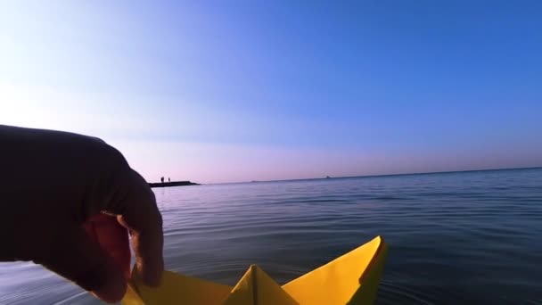 Kobieta umieszczenie żółtego papieru łódź na powierzchni wody fal morskich zbliżenie. — Wideo stockowe