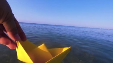 Sarı kağıt tekneyi deniz dalgalarının yüzeyine yakın çekim yapan bir kadın..