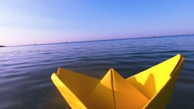 Sarı kağıttan tekne mavi deniz dalgalarının yüzeyinde yüzüyor..