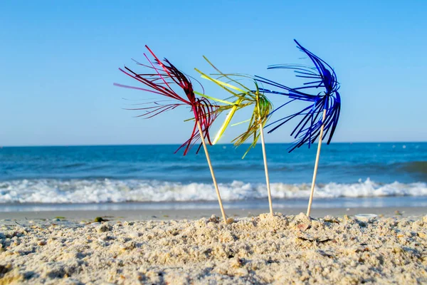 Três brilhantes decorações de coquetel coloridas no suporte de vara na areia perto do mar — Fotografia de Stock