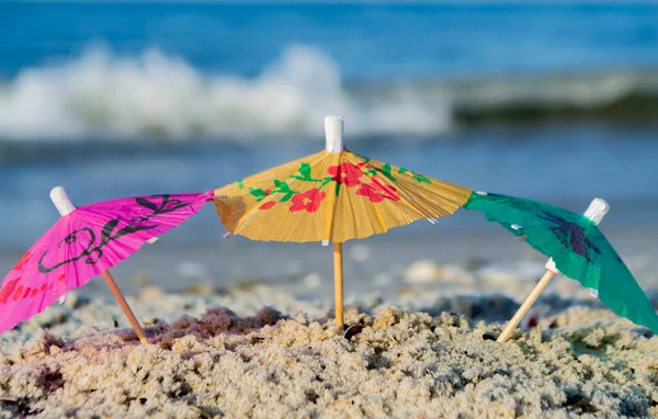 Trzy małe papierowe parasole stoją w piasku na piaszczystej plaży z bliska — Zdjęcie stockowe