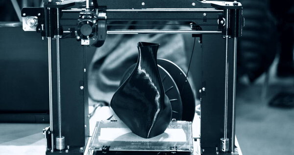 3D принтер печати модели в виде черной вазы крупным планом.
