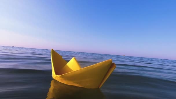 Κίτρινο χάρτινο σκάφος επιπλέει στην επιφάνεια των γαλάζιων νερών κύματα της θάλασσας close-up. — Αρχείο Βίντεο